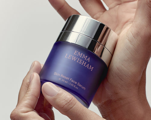 Hand holding a blue jar of Emma Lewisham Skin Reset Face Serum against a neutral background