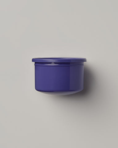 Purple refill pod for Supernatural Face Creme Riche with matching lid displayed on neutral gray background. Eco-friendly skincare container designed for product refills, showing sustainable packaging solution with simple cylindrical shape casting subtle shadow.